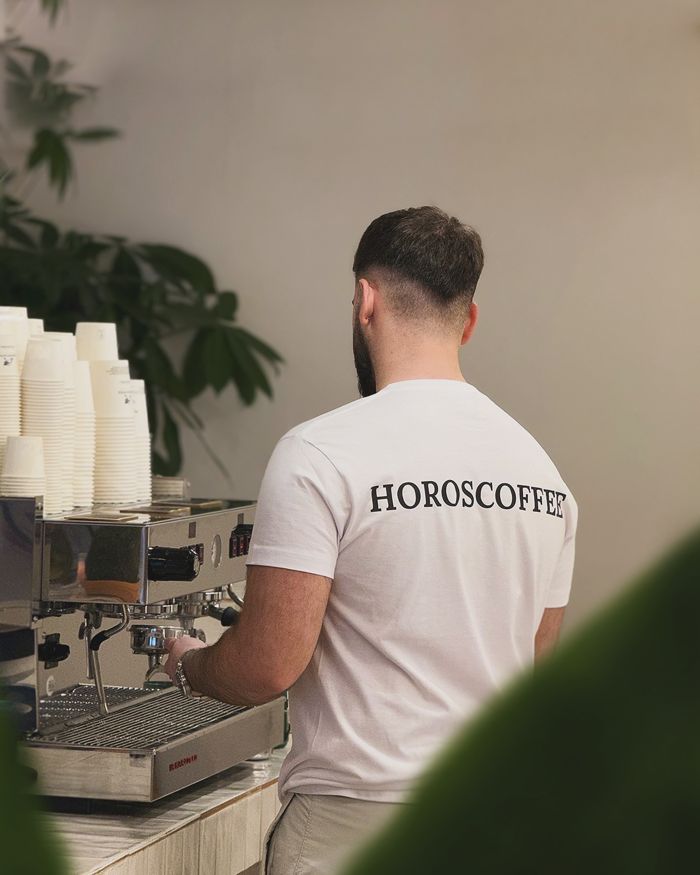 El barista, con la camiseta de HOROSCOFFEE, preparando café en la máquina