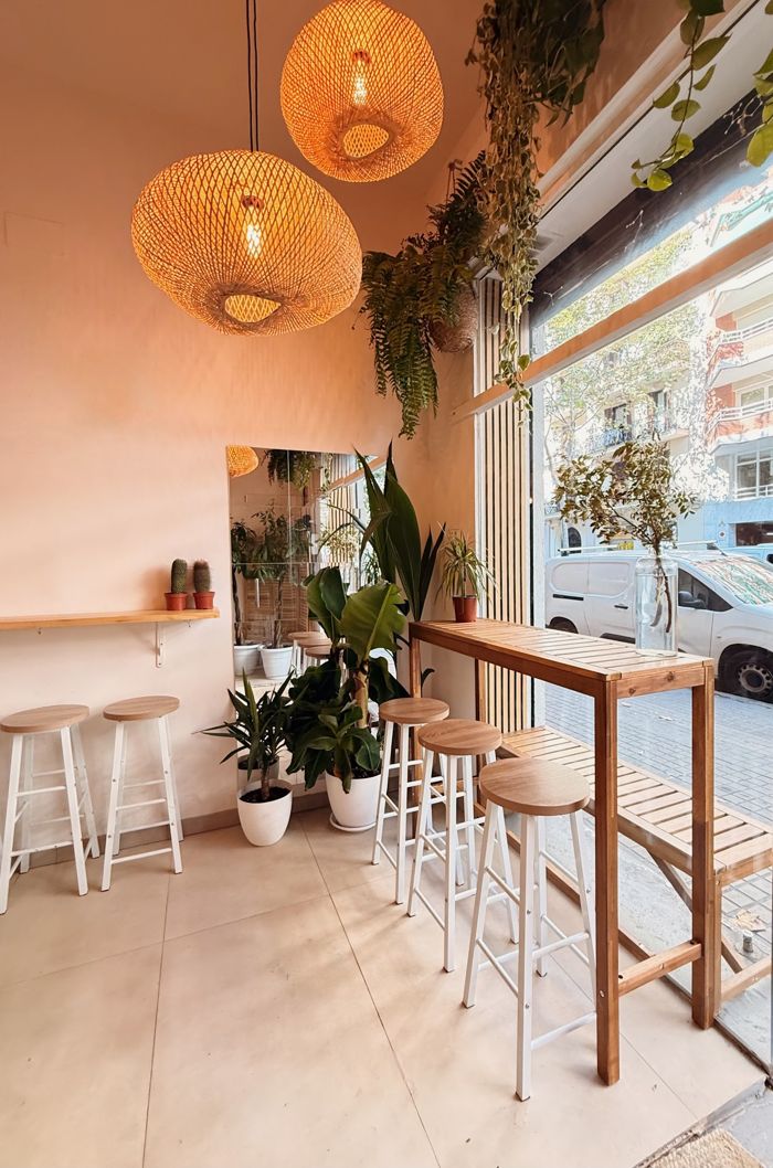 Taburetes de madera, plantas y lámparas de ratán junto al escaparate del café